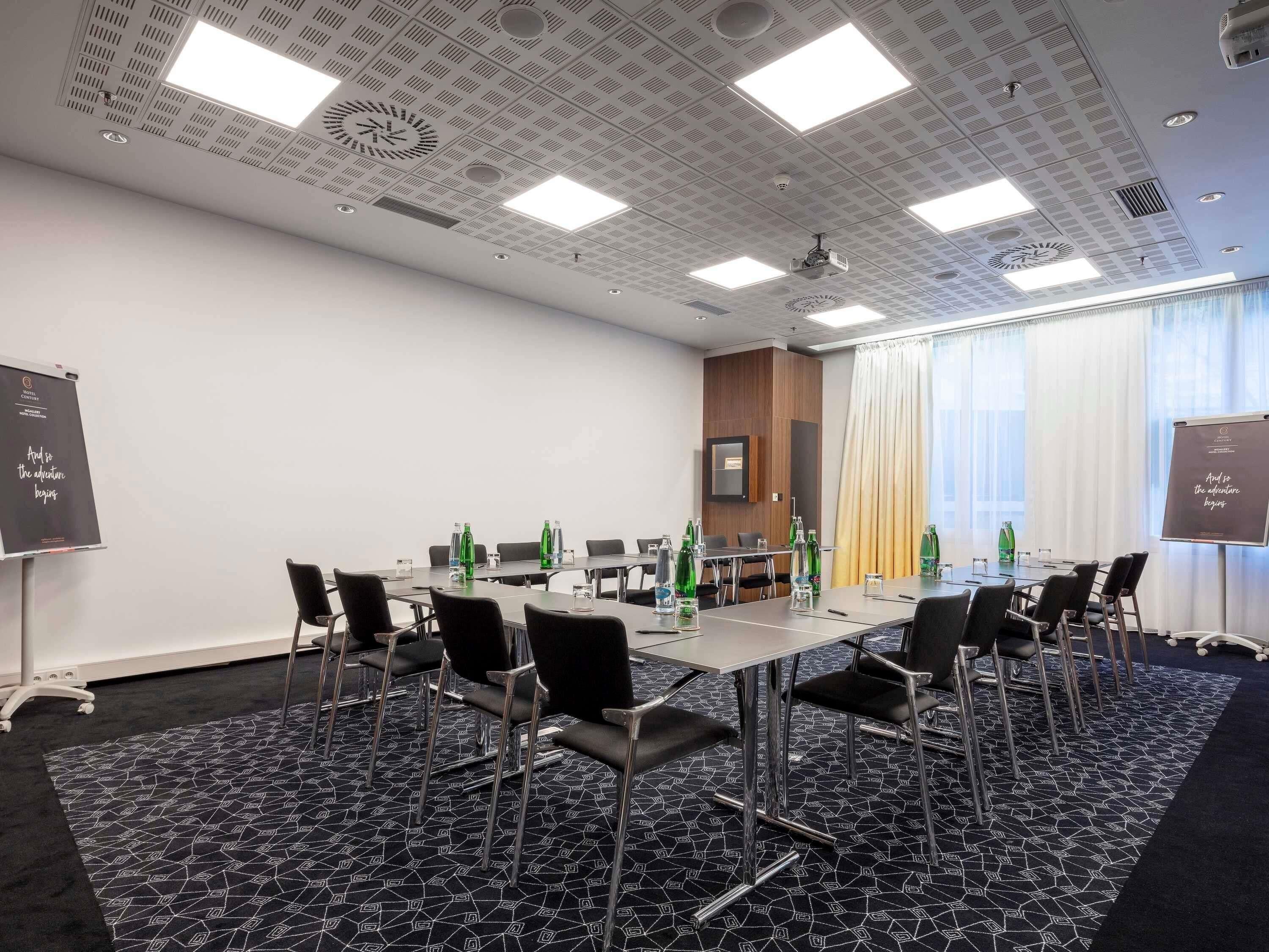 Een vergaderruimte met een lange tafel, stoelen, waterflesjes en een projectiescherm.