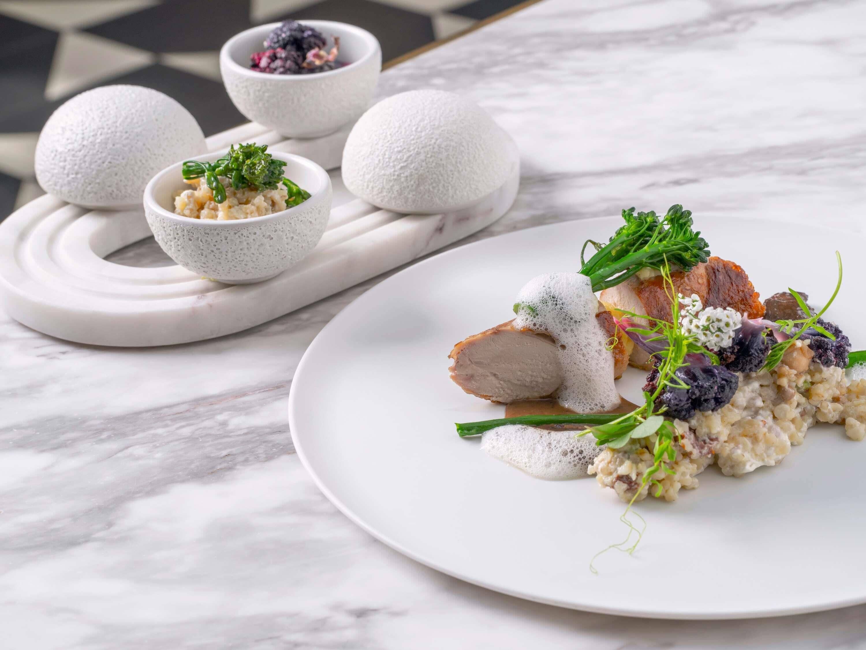 A white marble table with a plate of food, including meat and a creamy dish, and two bowls with a textured substance.
