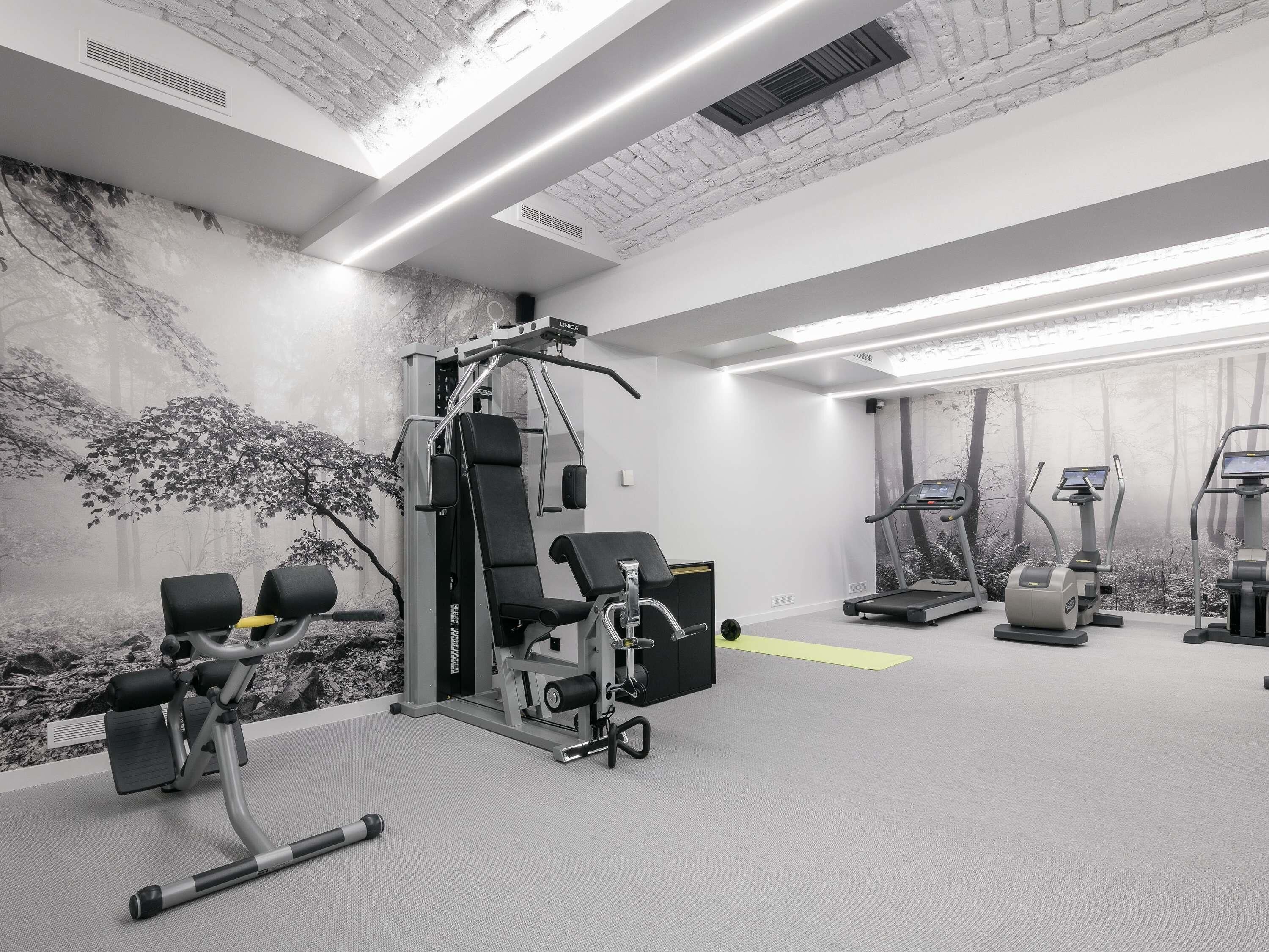 A gym with exercise equipment, a wall mural, and a ceiling with exposed brick.