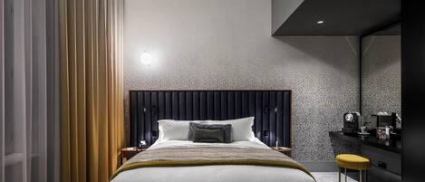 Un dormitorio moderno con una cama grande, un cabecero oscuro, una mesita de noche y un pequeño taburete.