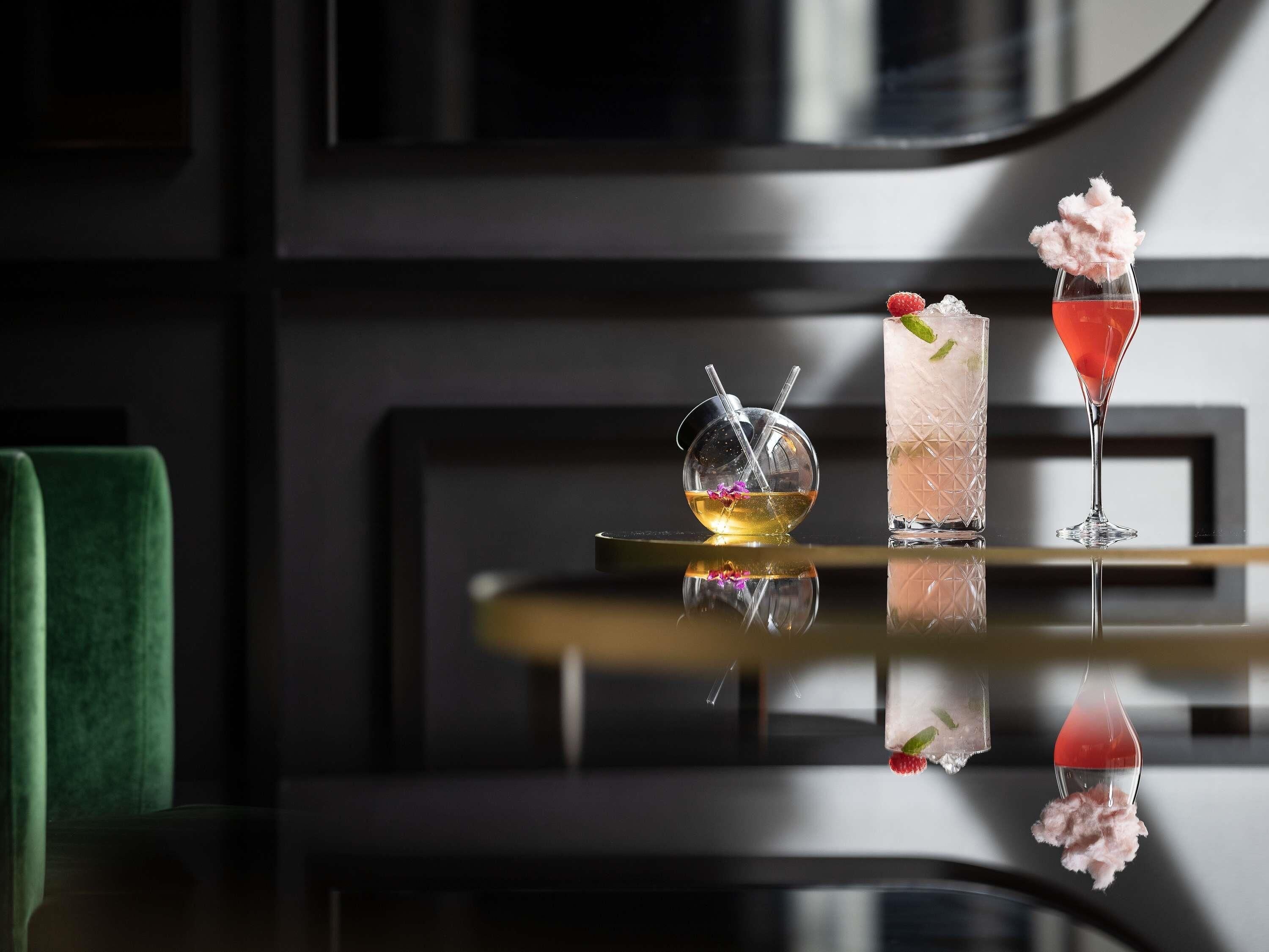 Een bar met drie drankjes, een groene stoel en een reflecterend oppervlak.