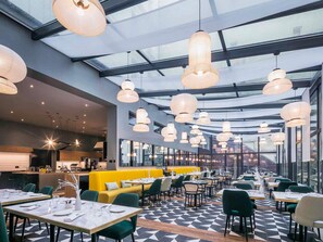 Un restaurante moderno con techo alto, ventanas amplias y múltiples lámparas colgantes.
