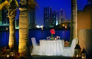 An outdoor dining setup with a table, chairs, candles, and a flower centerpiece.