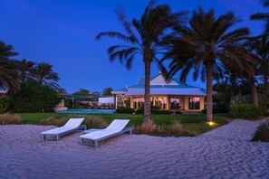 A beachside resort with a pool, palm trees, and lounge chairs.