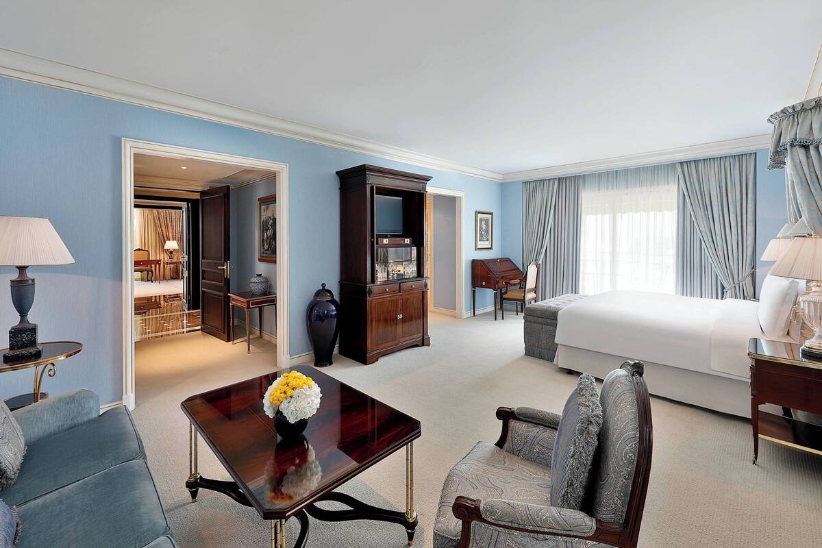A hotel room with a bed, a sitting area with a table and chairs, a television, and a dining area with a table and chairs.