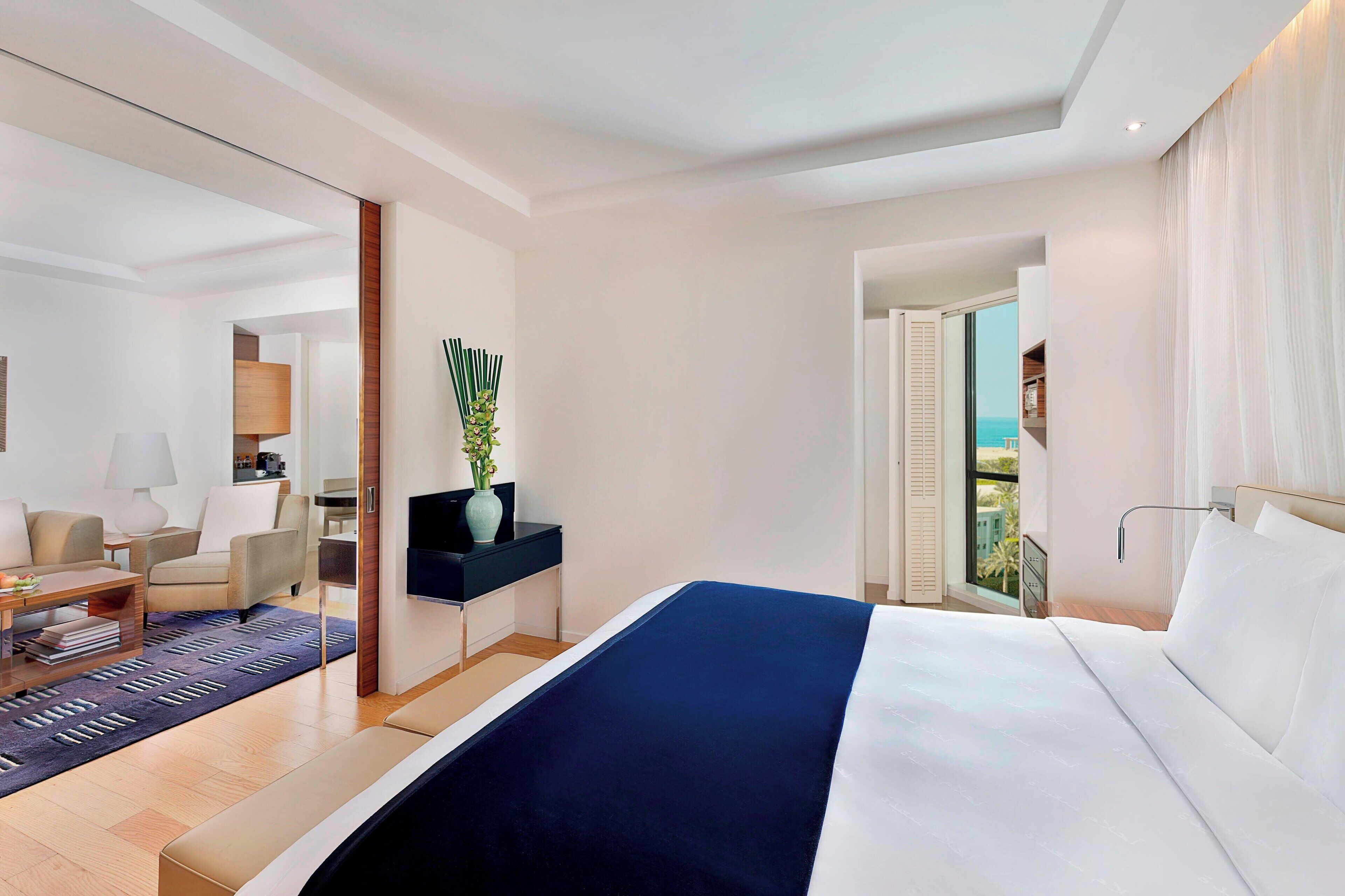 Una habitación de hotel moderna con una cama grande, un escritorio, una silla, una lámpara y vistas al exterior.