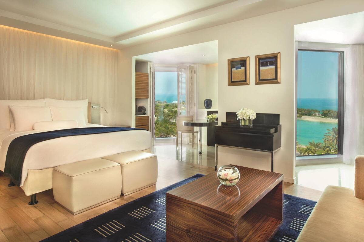 A modern hotel room with a large bed, a desk, and a view of the ocean.