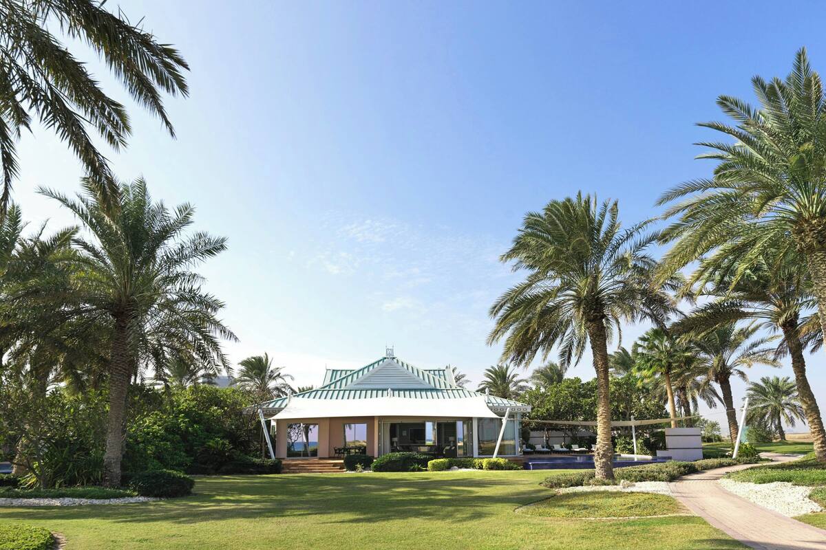A building with a green roof, surrounded by palm trees and a well-maintained lawn.