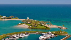 A marina with boats docked, a sandy beach, and a landscaped island with palm trees.
