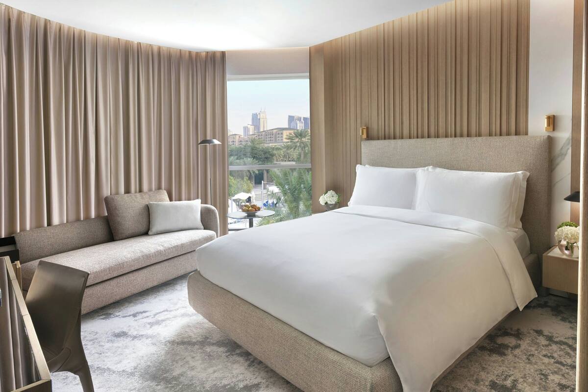 A modern hotel room with a large bed, a sofa, a desk, and a view of the cityscape.