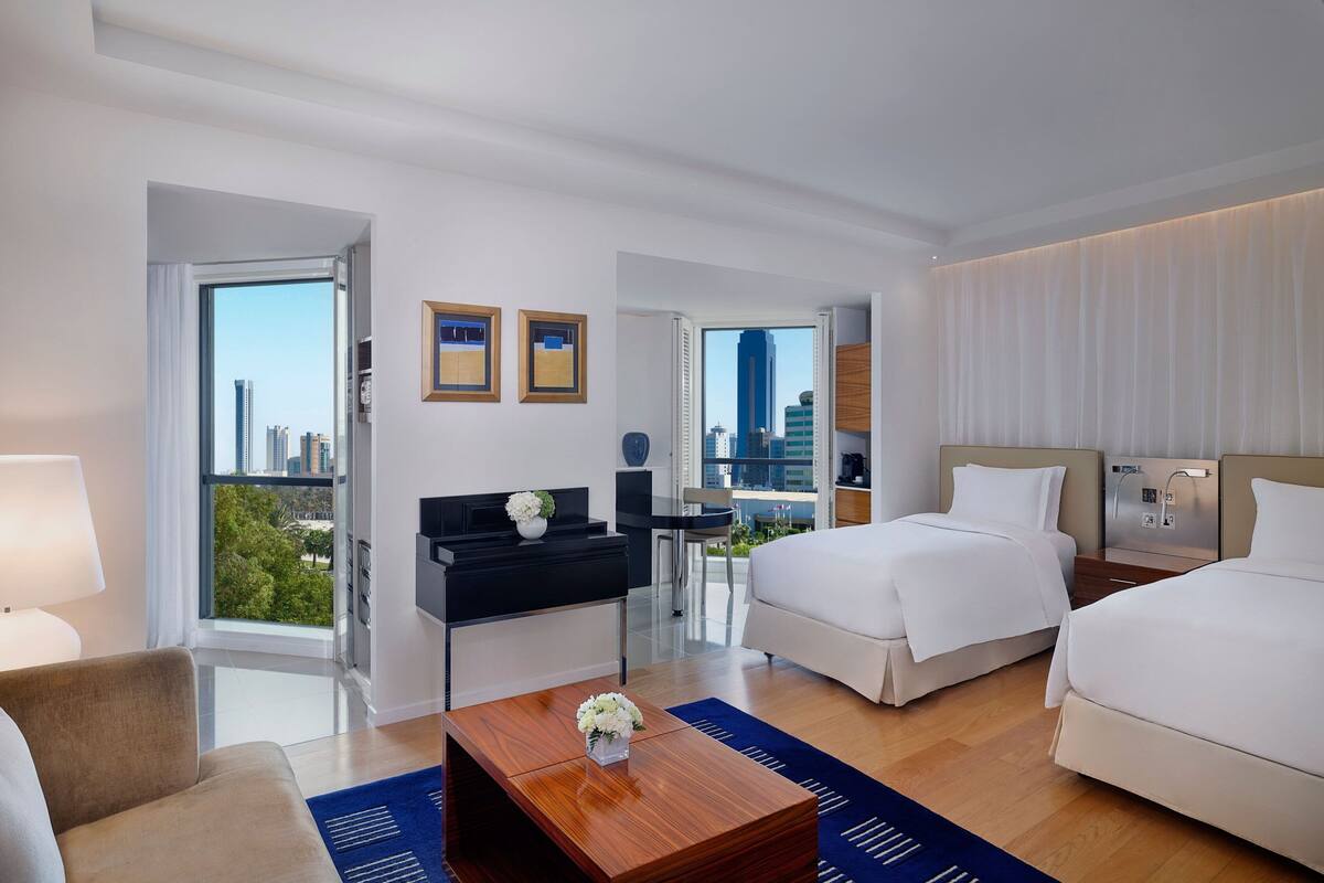 A modern hotel room with a large bed, a desk, and a view of the cityscape.