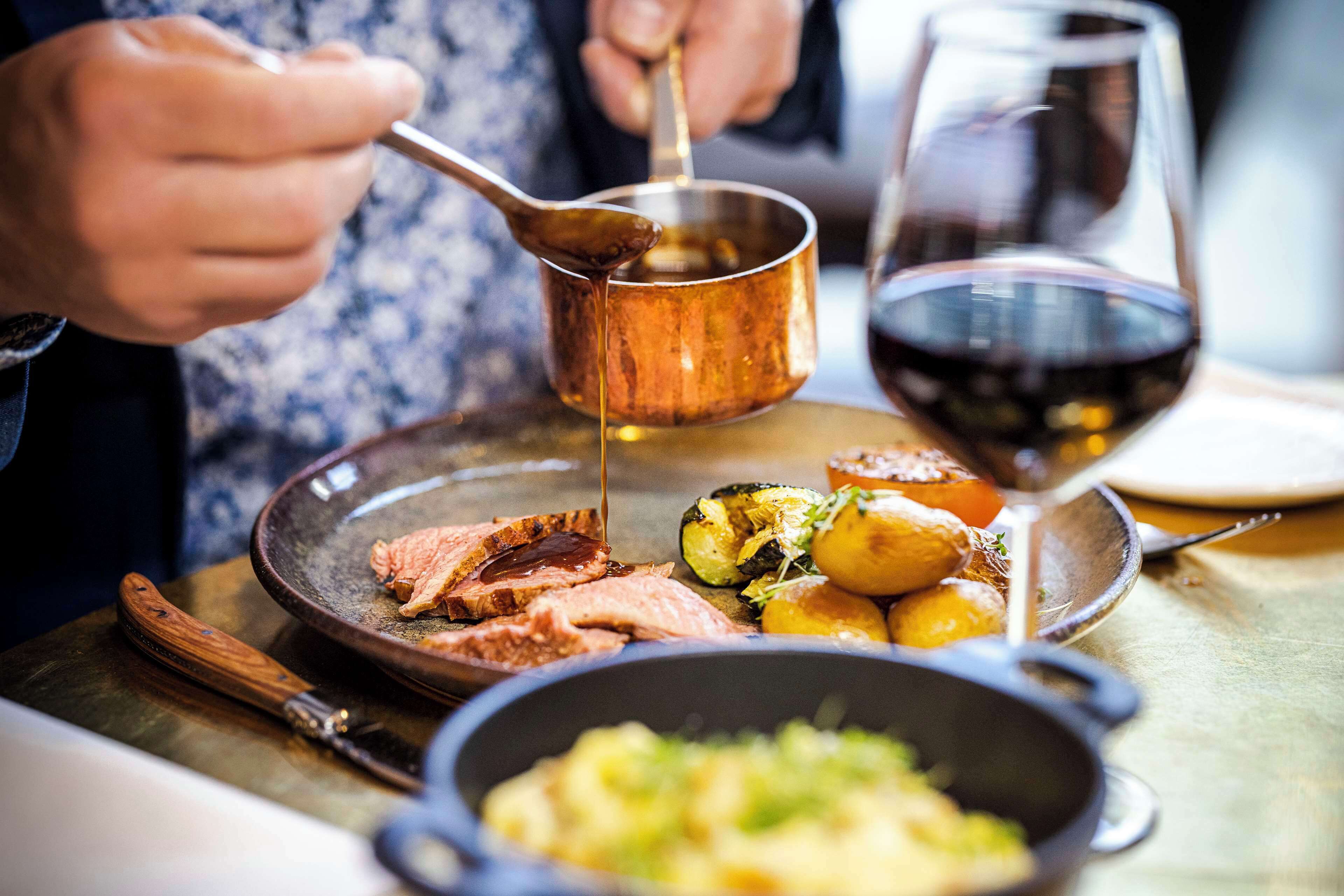 A dining table with a meal consisting of sliced meat, roasted vegetables, and a bowl of mashed potatoes.