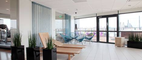 A modern lounge area with black planters, wooden lounge chairs, and blue chairs.