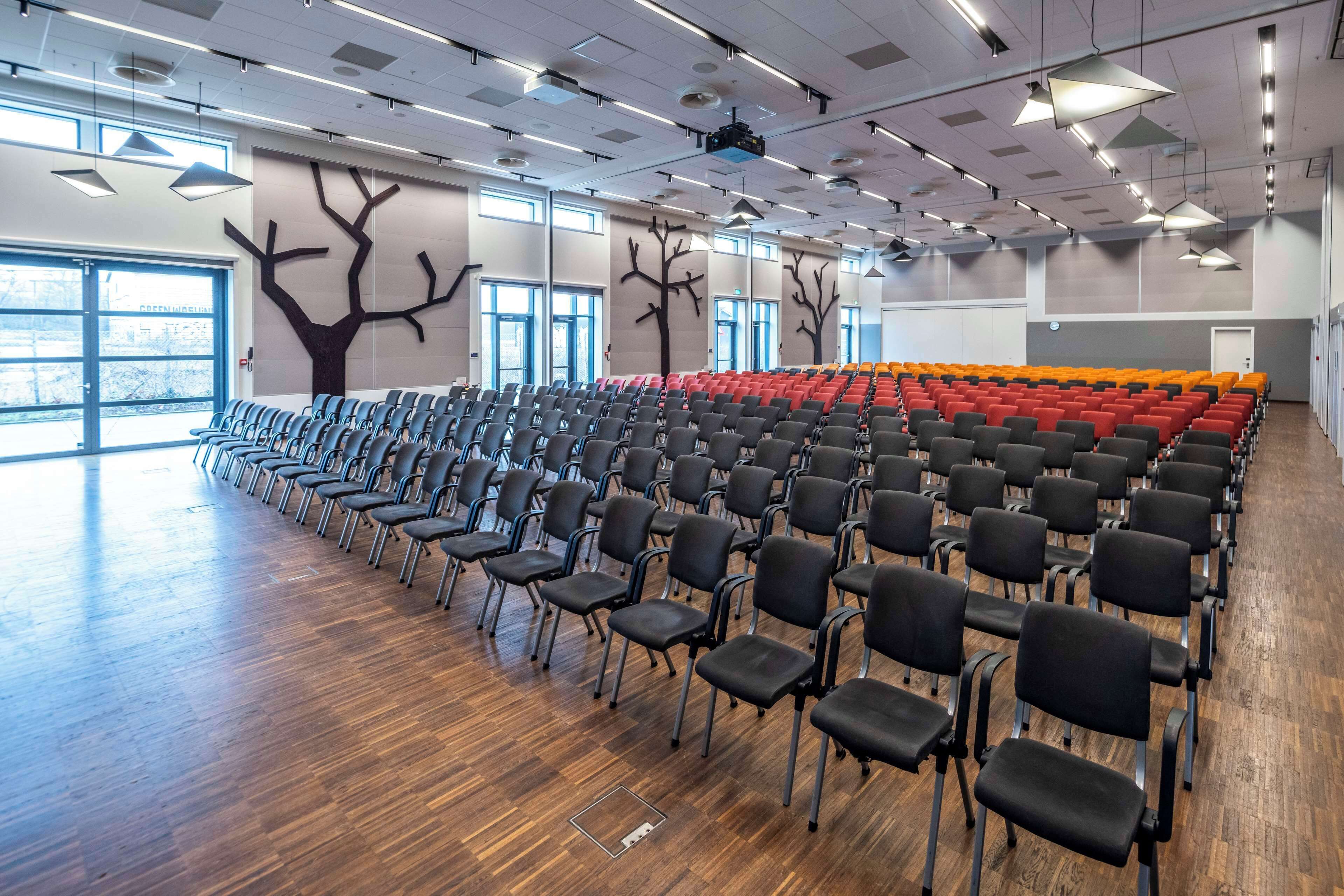 A conference room with rows of chairs, a large window, and tree-shaped wall decorations.