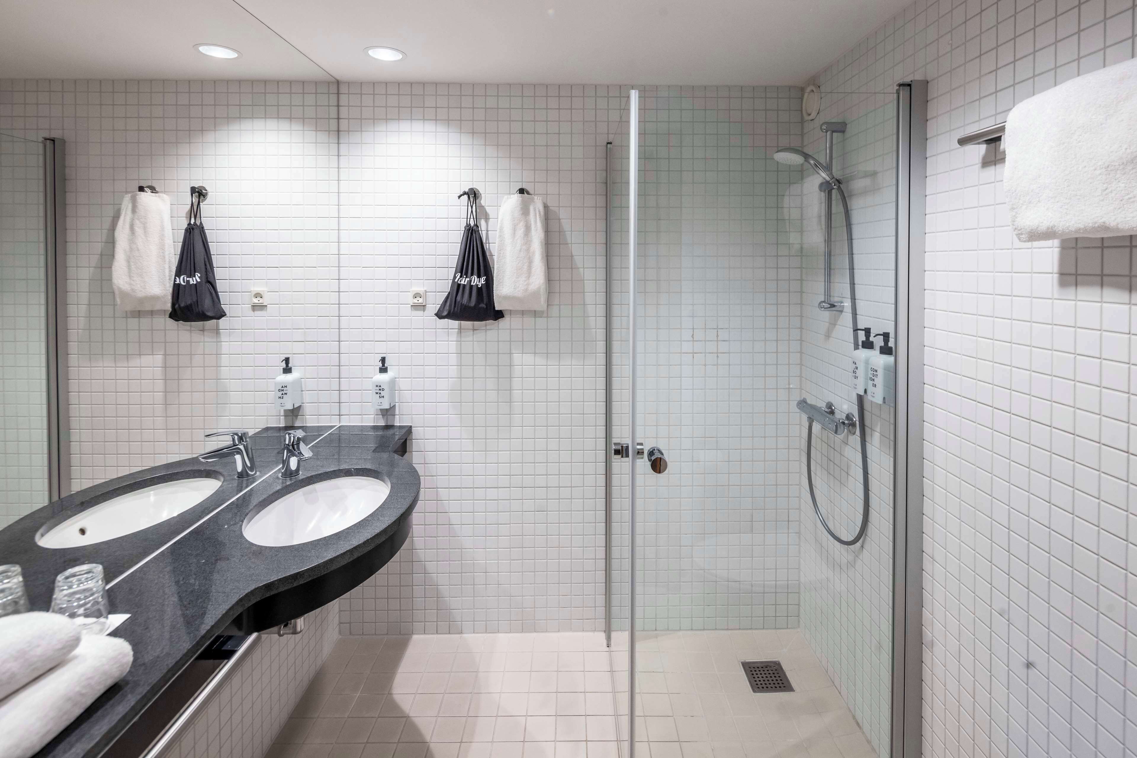 Une salle de bain moderne avec deux vasques, une douche en verre et deux serviettes suspendues à des crochets.