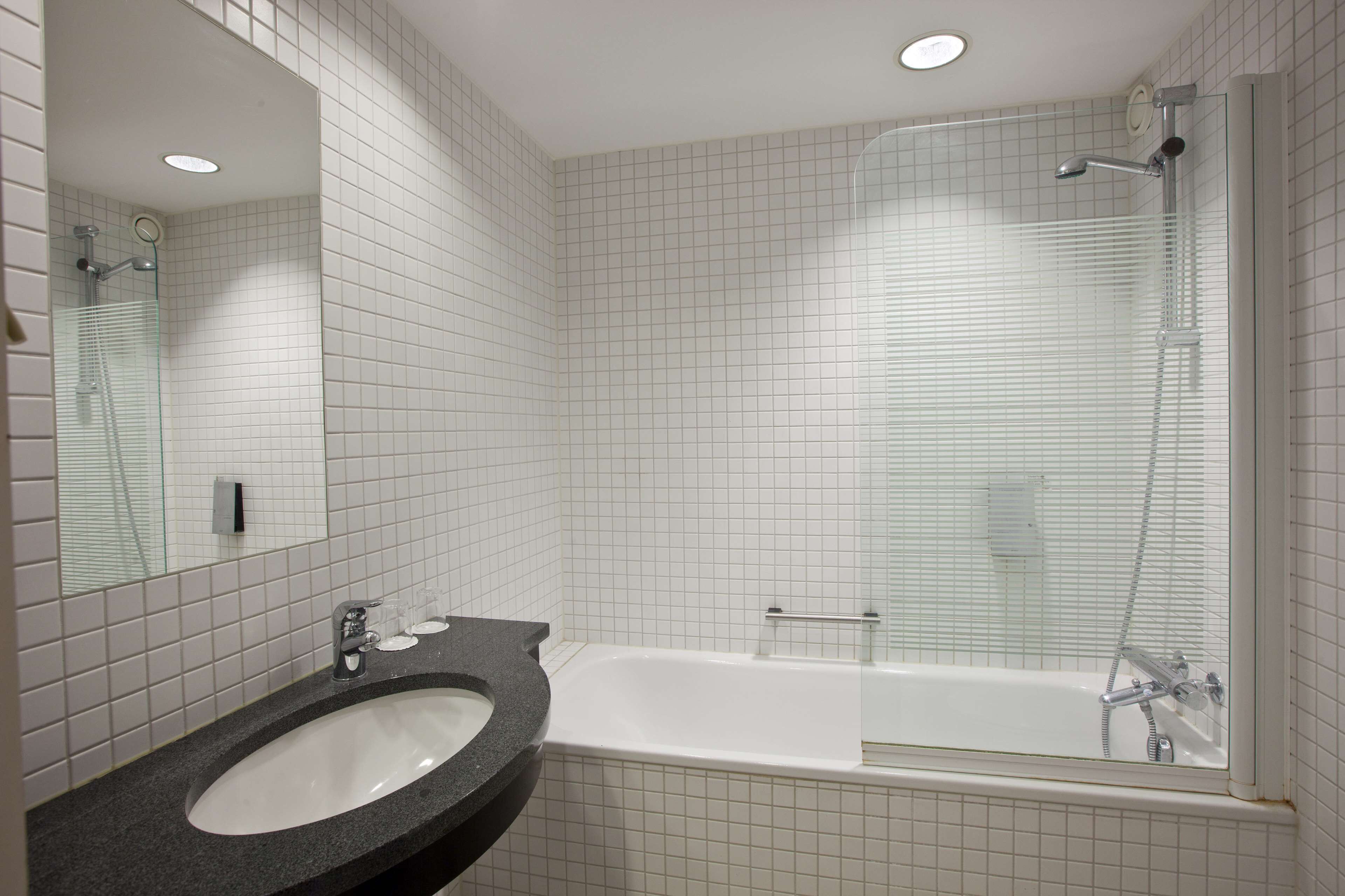 Un baño con pared de azulejos blancos, un lavamanos negro y una bañera blanca.
