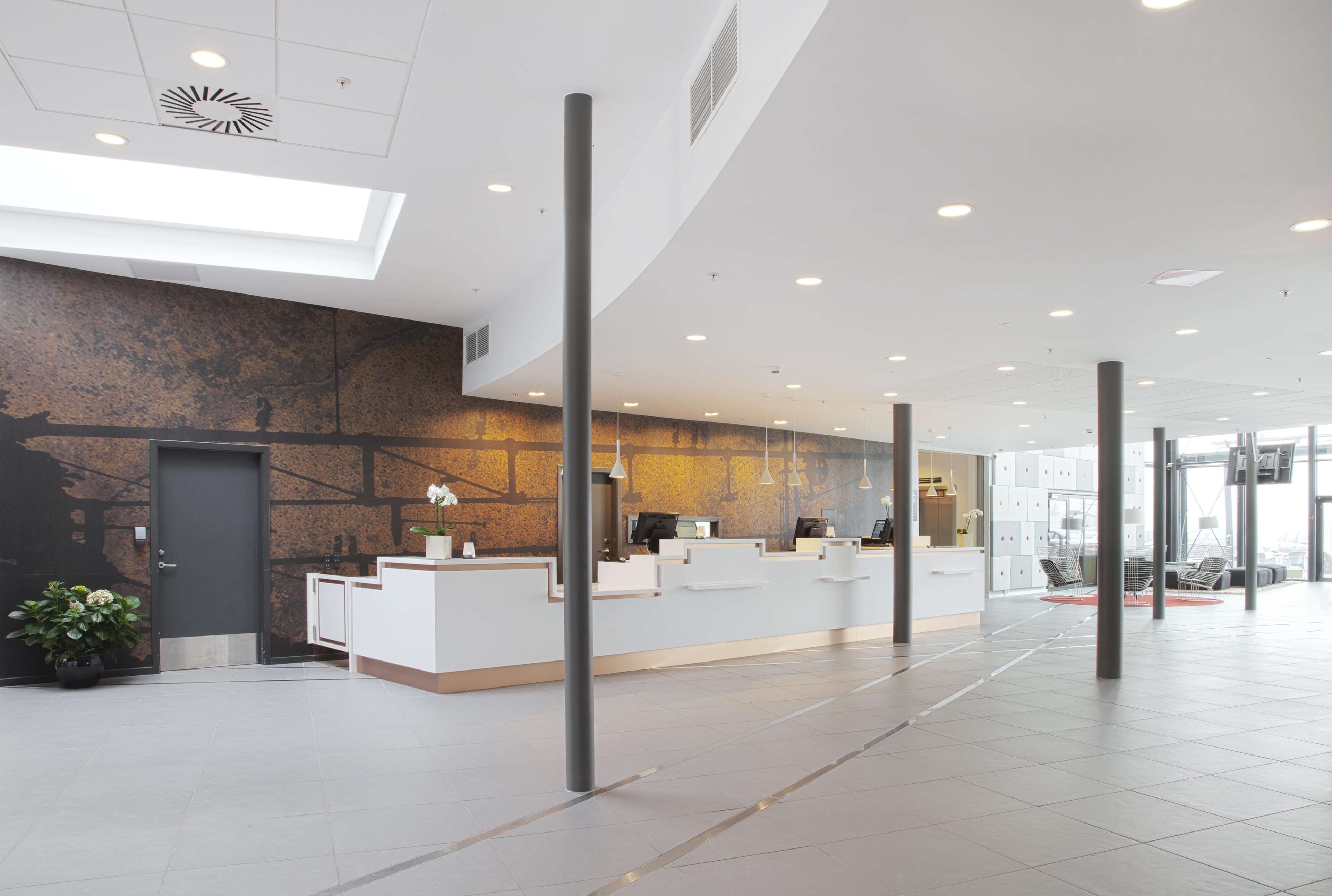 Zona d'entrada moderna amb taulell de recepció blanc, una finestra gran i un sostre alt amb il·luminació empotrada.
