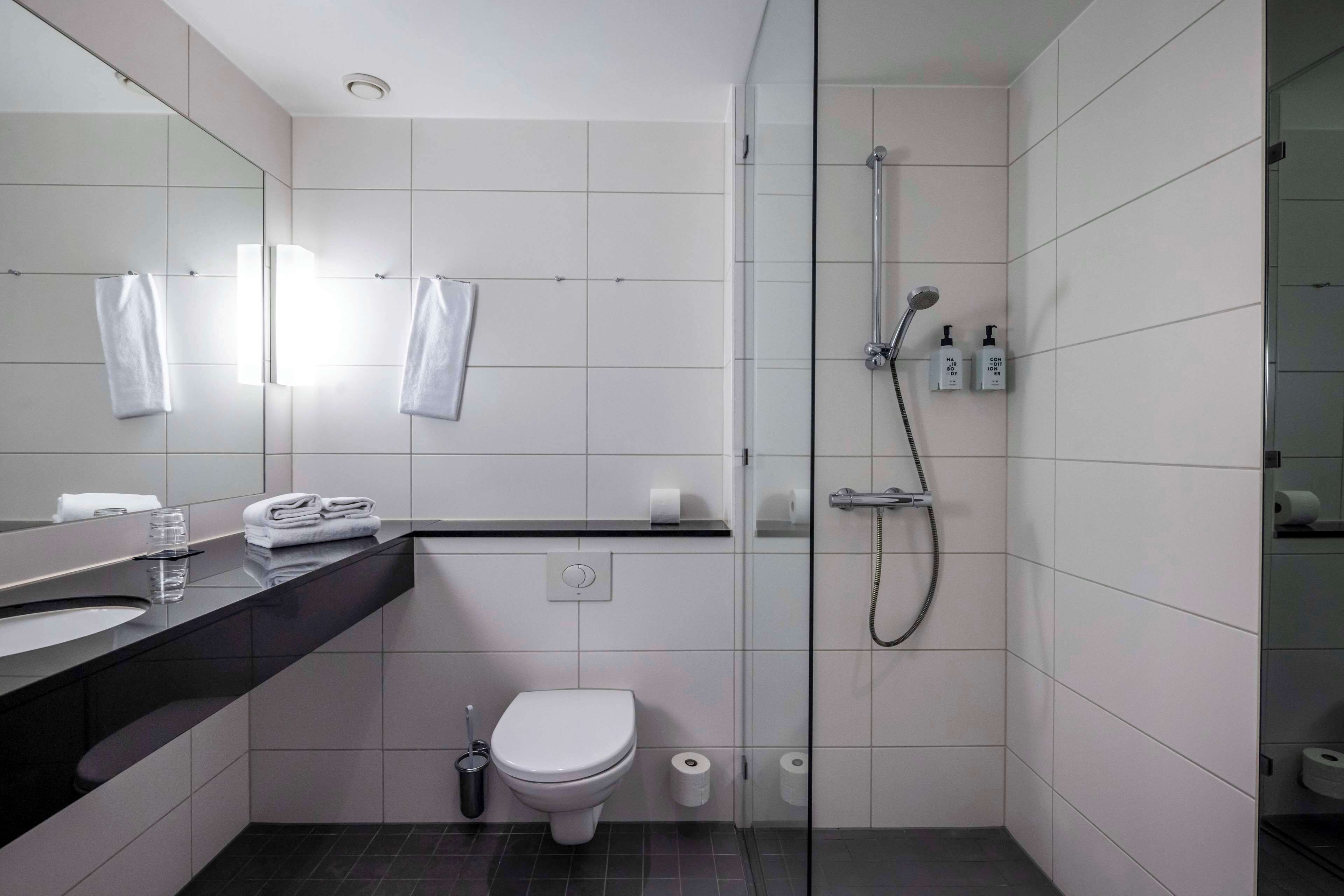 A modern bathroom with a glass-enclosed shower, a black countertop sink, and a white toilet.