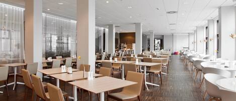 A spacious dining area with multiple tables and chairs, large windows, and a modern interior design.