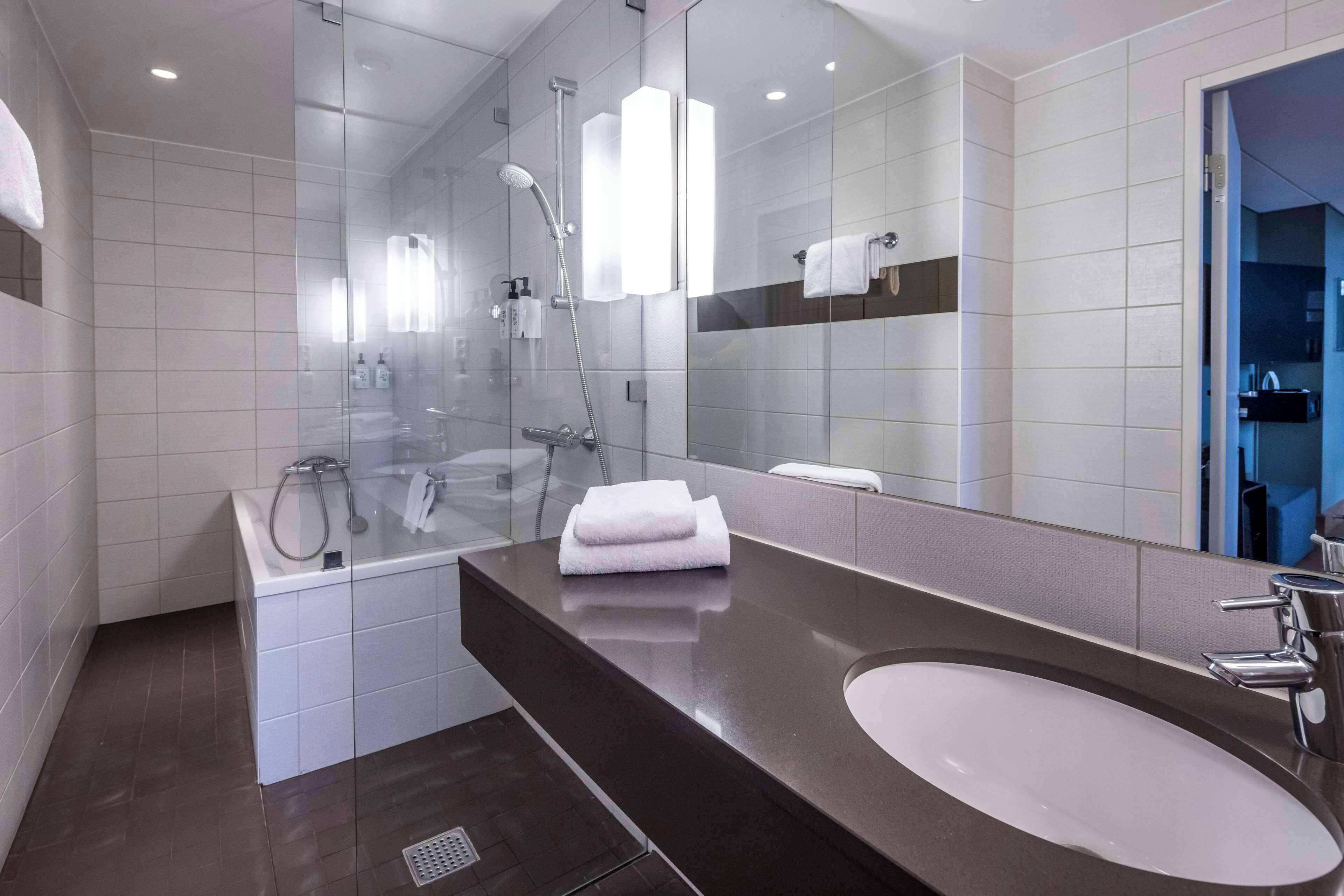A modern bathroom with a glass-enclosed shower, a large mirror, a dark countertop, and a white sink.