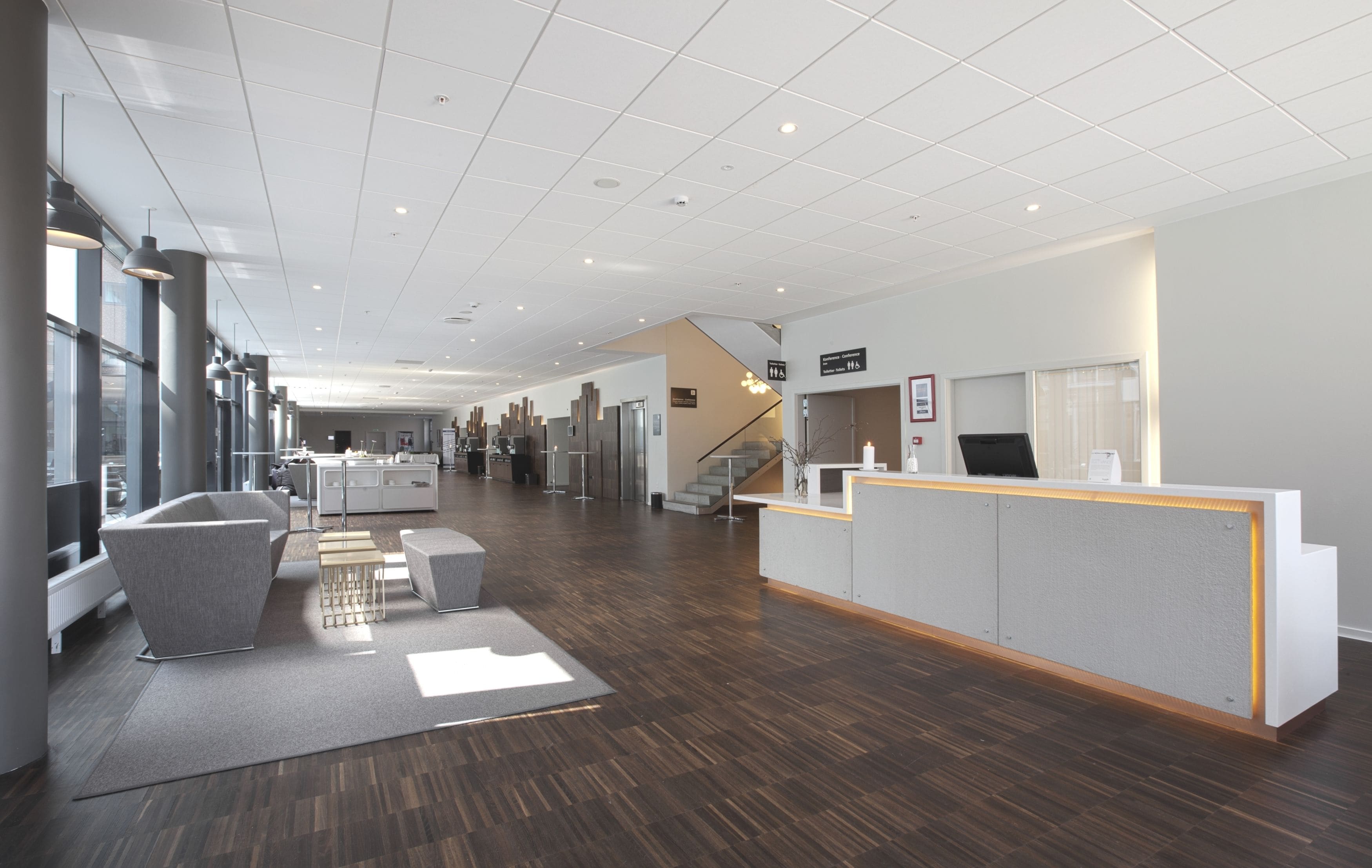 A modern hotel lobby with a reception desk, seating area, and a staircase leading to upper floors.