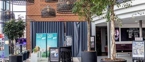 A modern indoor area with hanging lamps, seating, and informational posters.