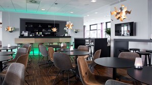 A modern restaurant with round tables and chairs, a bar area, and a flat-screen TV mounted on the wall. - Scandic Sydhavnen (Copenhagen)