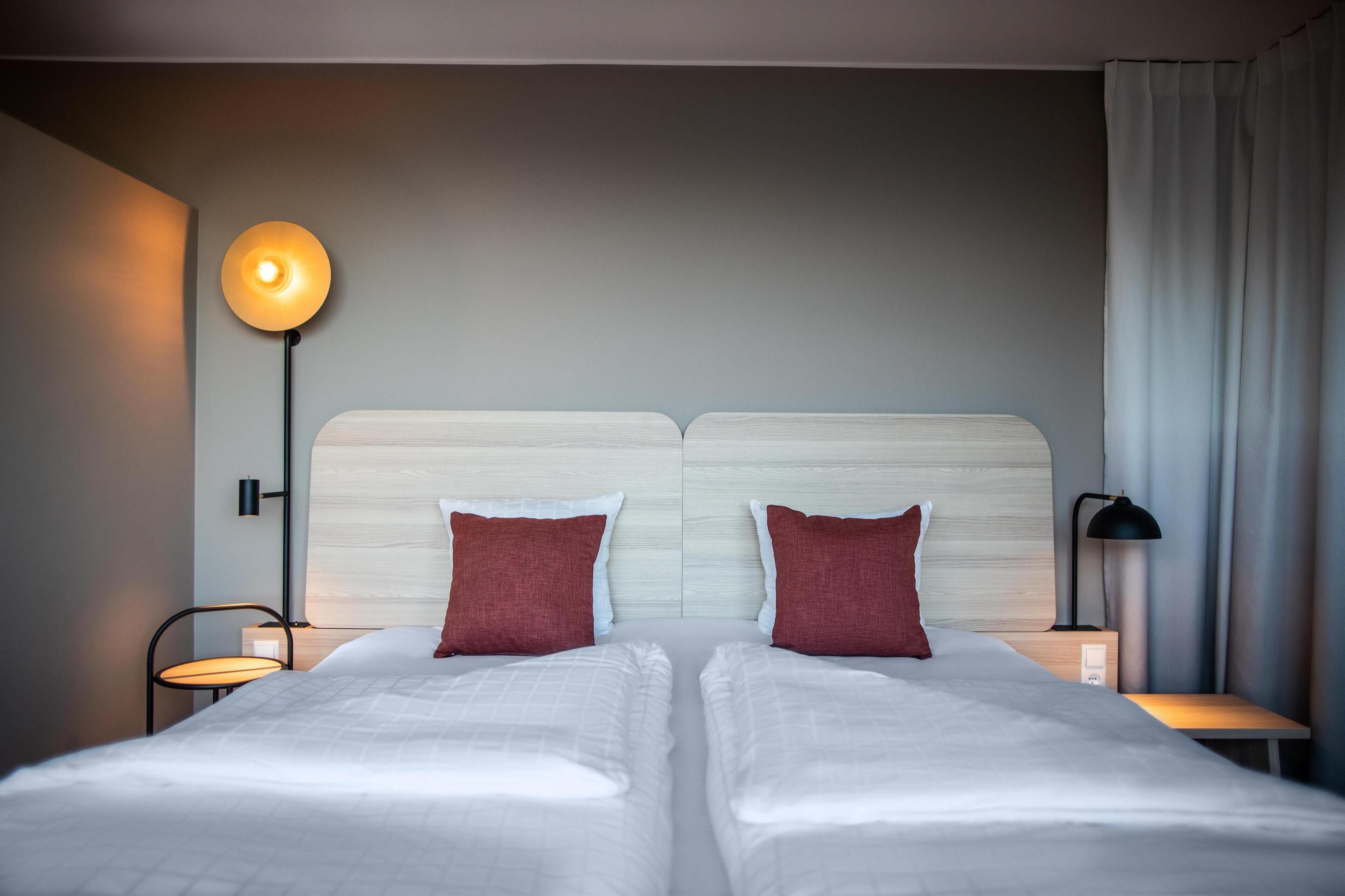 Habitación de hotel con dos camas, cabeceros, lámparas de noche y una lámpara de pared.