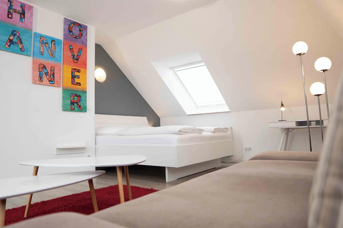 A modern bedroom with a sloped ceiling, a skylight, a white bed, a red rug, and a small round table.
