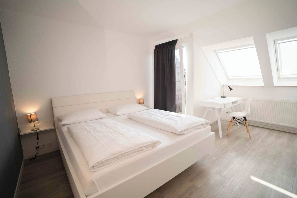 A modern bedroom with a large bed, a desk, and a window.