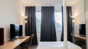 A hotel room with a bed, a desk with a chair, a TV, and a window with curtains. - Plaza Inn Hannover City Nord (Hannover)