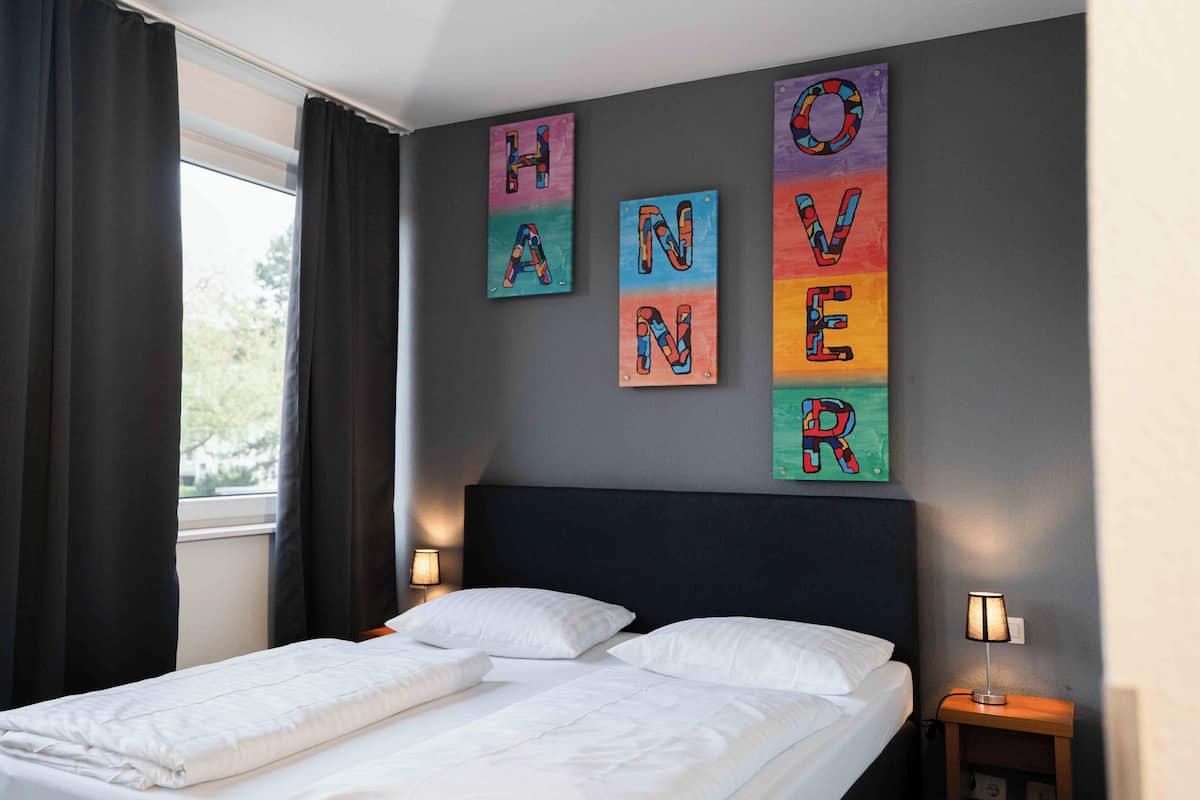 A neatly made bed with white linens, a dark headboard, and two bedside lamps.