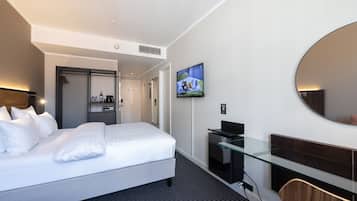 Ett modernt hotellrum med en stor säng, ett skrivbord, en TV och en spegel.
