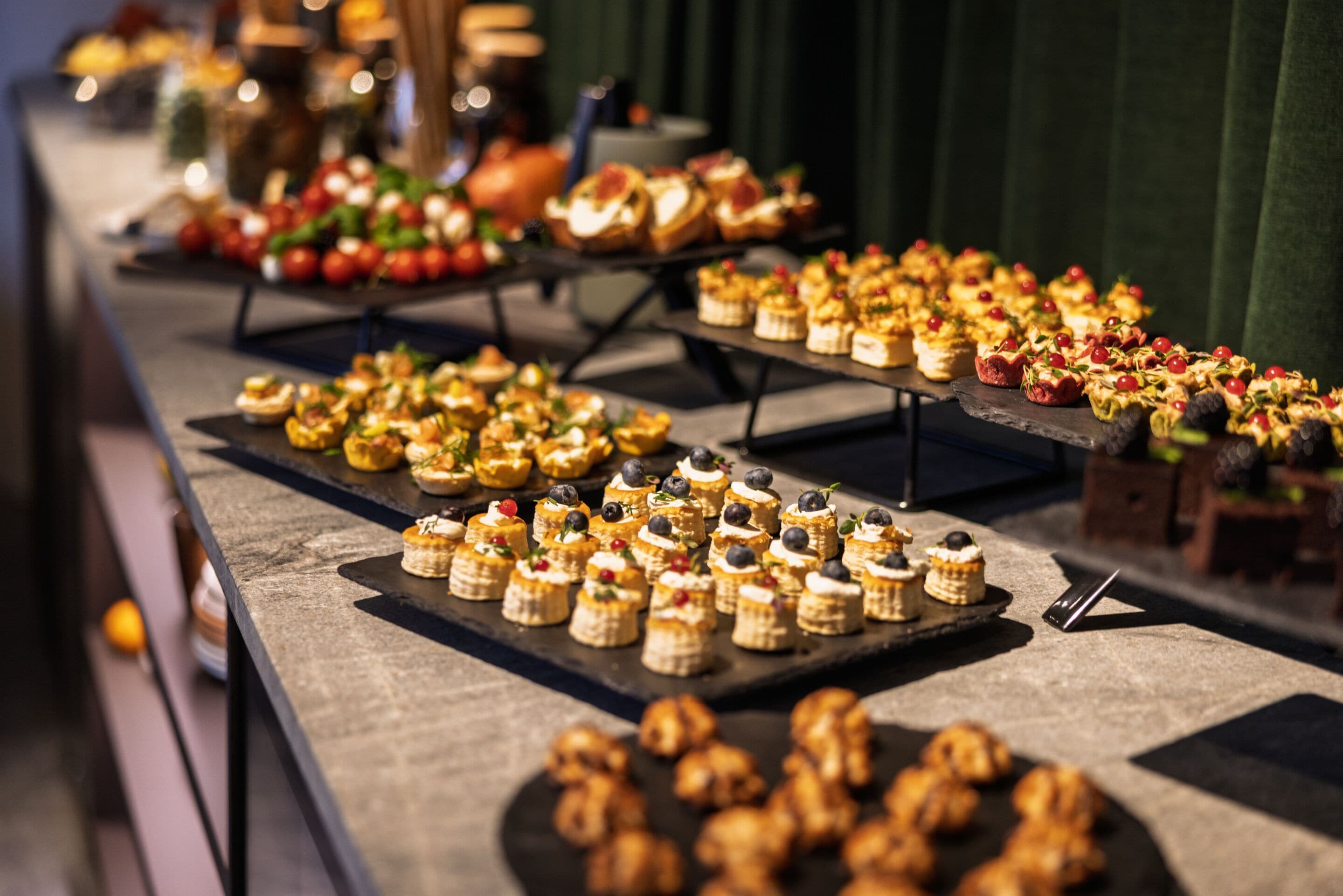 A buffet with various food items, including pastries and fruits, arranged on multiple serving boards.