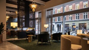 A modern lobby with a green carpet, seating area, and large windows offering views of the street. - The Square (Copenhagen)