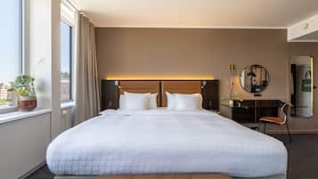 A hotel room with a large bed, a desk, a chair, a mirror, and a window with a view of buildings.