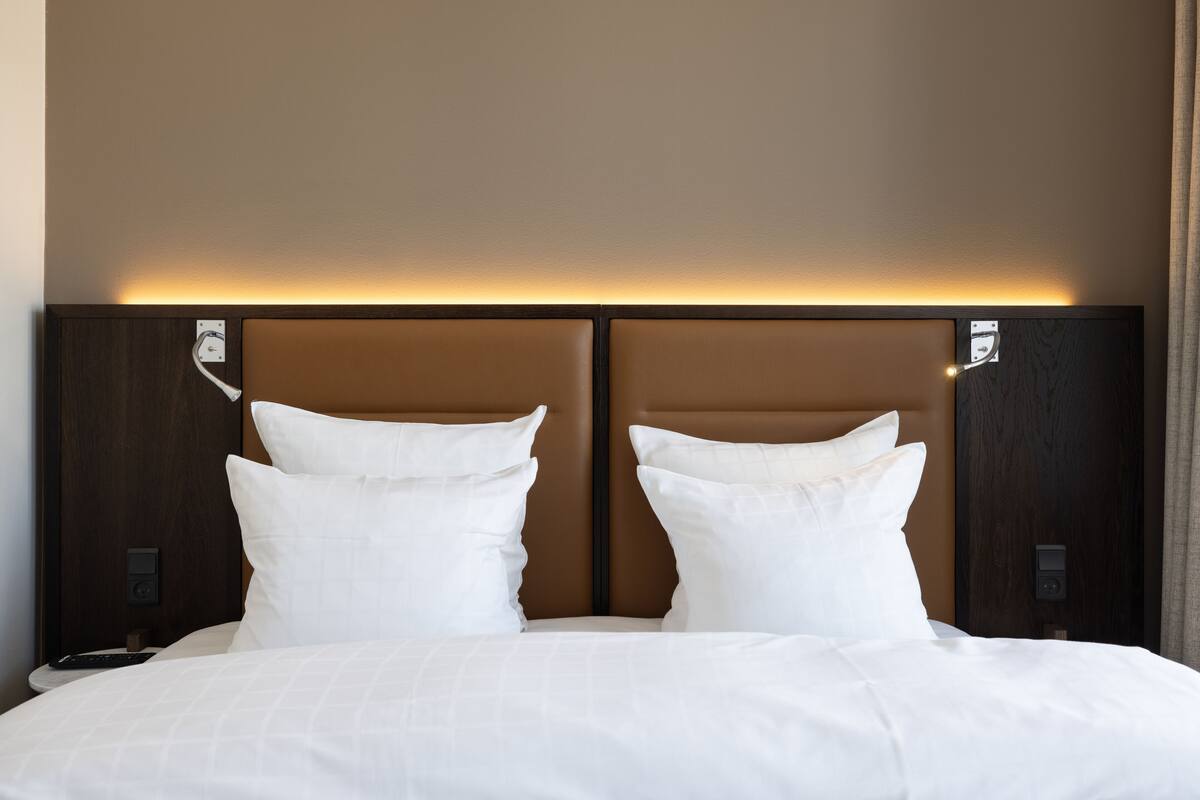 A hotel room with a large bed, two white pillows, a wooden headboard, and a bedside table with a remote control.