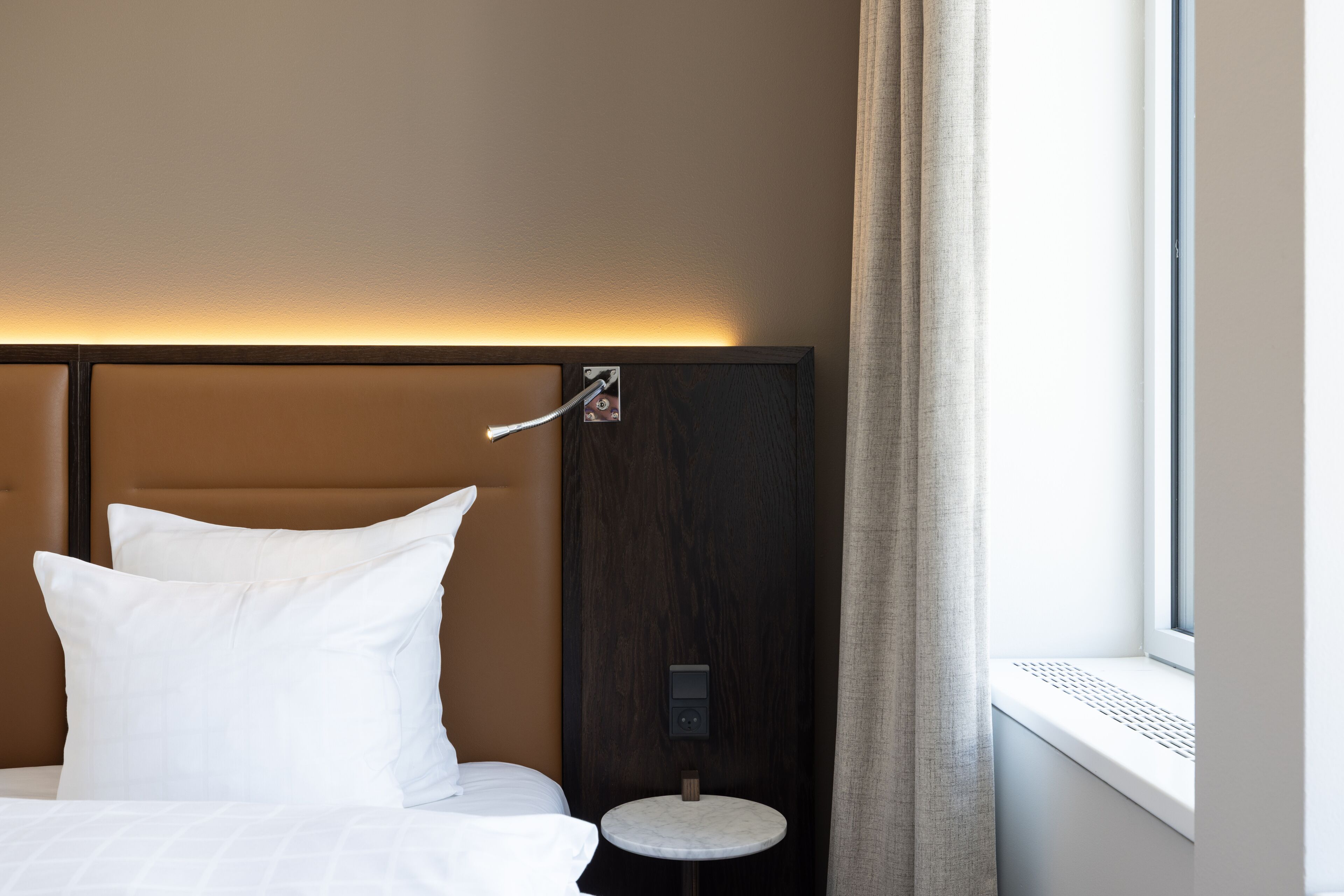 Et hotelværelse med en seng, et lille natbord og et vindue med gardiner.