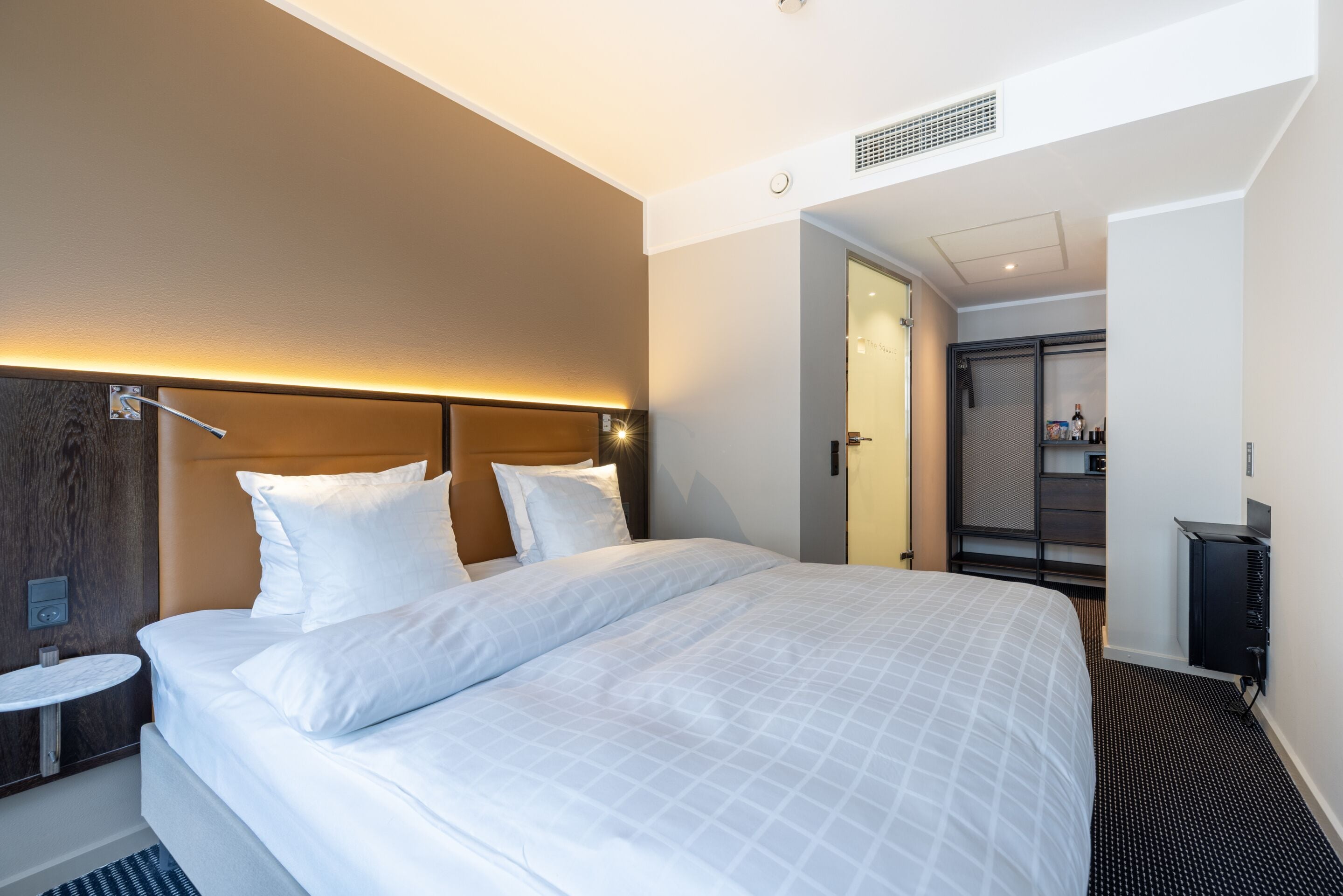 A hotel room with a large bed, a bedside table, a wardrobe, and a bathroom visible through an open door.