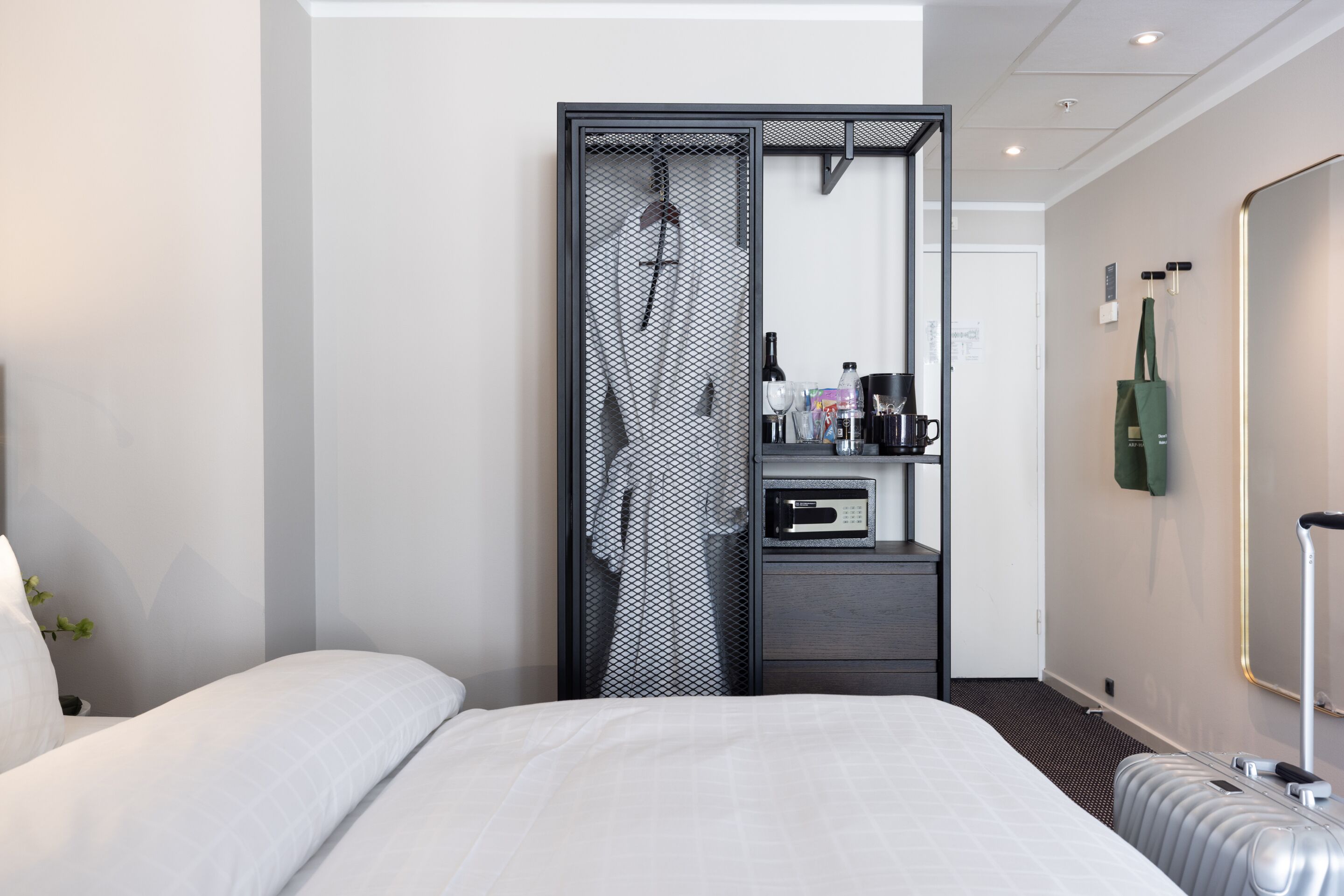 A modern hotel room with a large bed, a walk-in closet, a minibar, and a mirror.