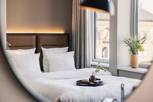 A hotel room with a large bed, a window with curtains, and a plant on the windowsill.