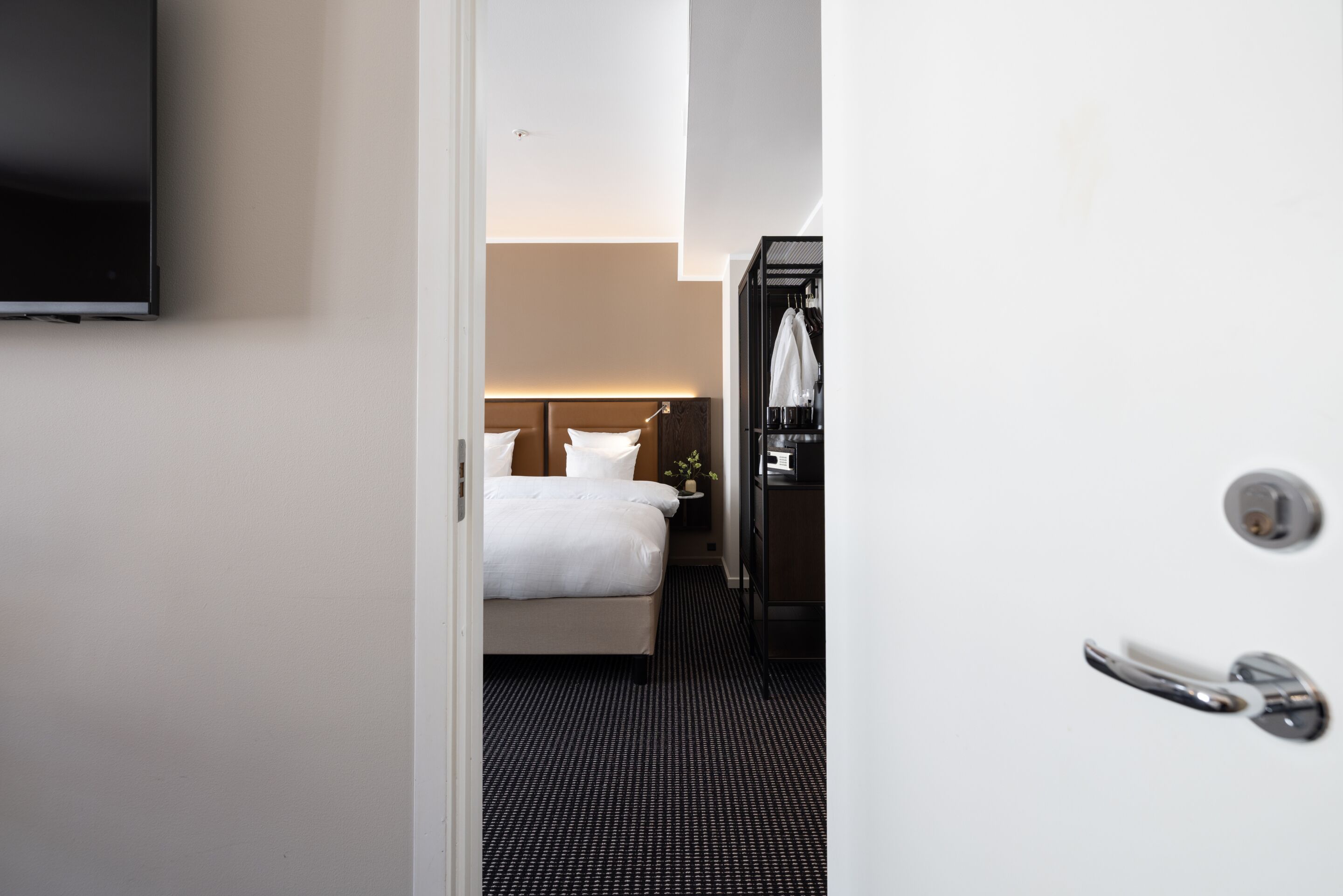 A hotel room with a bed, a TV mounted on the wall, a wardrobe, and a door with a handle.