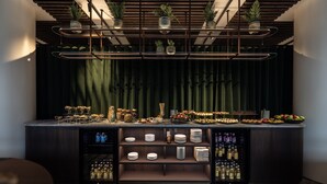 A bar area with a dark curtain backdrop, shelves with plates, glasses, and bottles, and hanging plants. - The Square (Copenhagen)