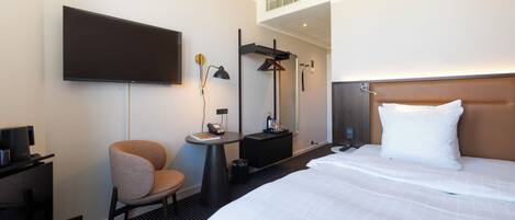 Una habitación de hotel con una cama, una silla, un escritorio, un televisor y un espejo.