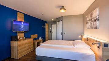 A modern bedroom with a large bed, a wooden dresser, a flat-screen TV, and a wall-mounted light fixture.