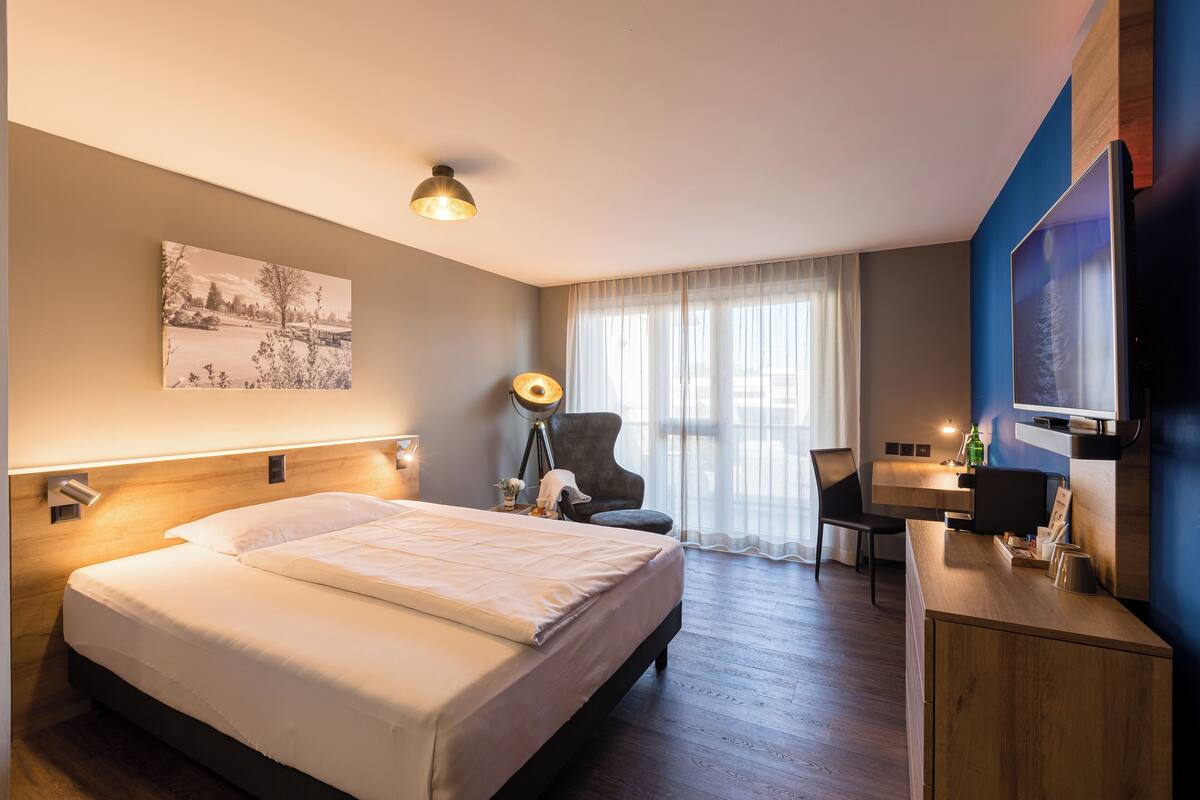 Una habitación de hotel con cama, escritorio, silla, lámpara y televisor.