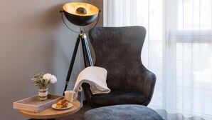 A modern room with a dark armchair, a floor lamp, a tray with a cup and croissant, and a vase with flowers. - Hotel aarau-WEST (Oberentfelden)