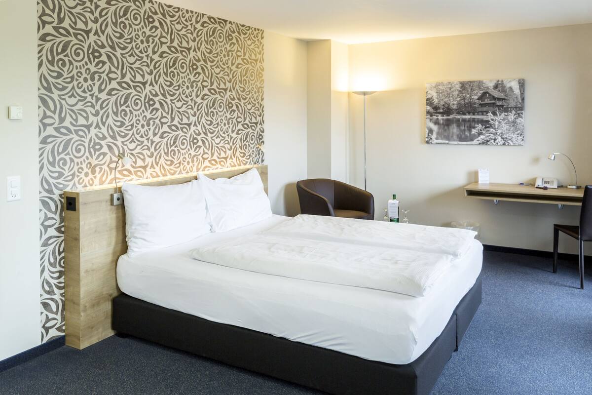 Una habitación de hotel con una cama grande, un escritorio con silla, una lámpara y un cuadro en la pared.