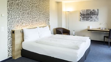 Una habitación de hotel con una cama grande, un escritorio con silla, una lámpara y un cuadro en la pared.