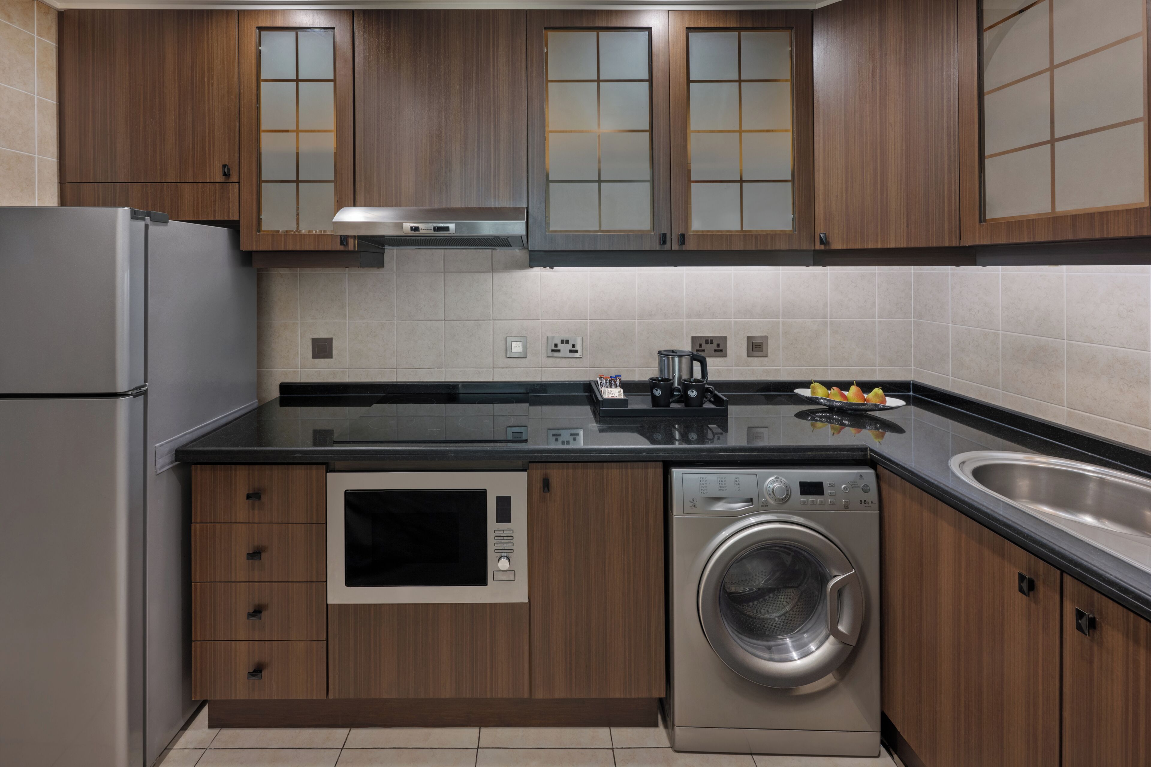Een moderne keuken met houten kastjes, een roestvrijstalen koelkast, een inbouwoven, een wasmachine en een spoelbak.